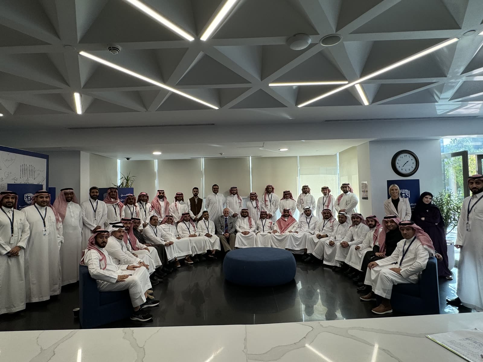 A large leadership cohort gathered with Robert Hausmann in an atrium setting.